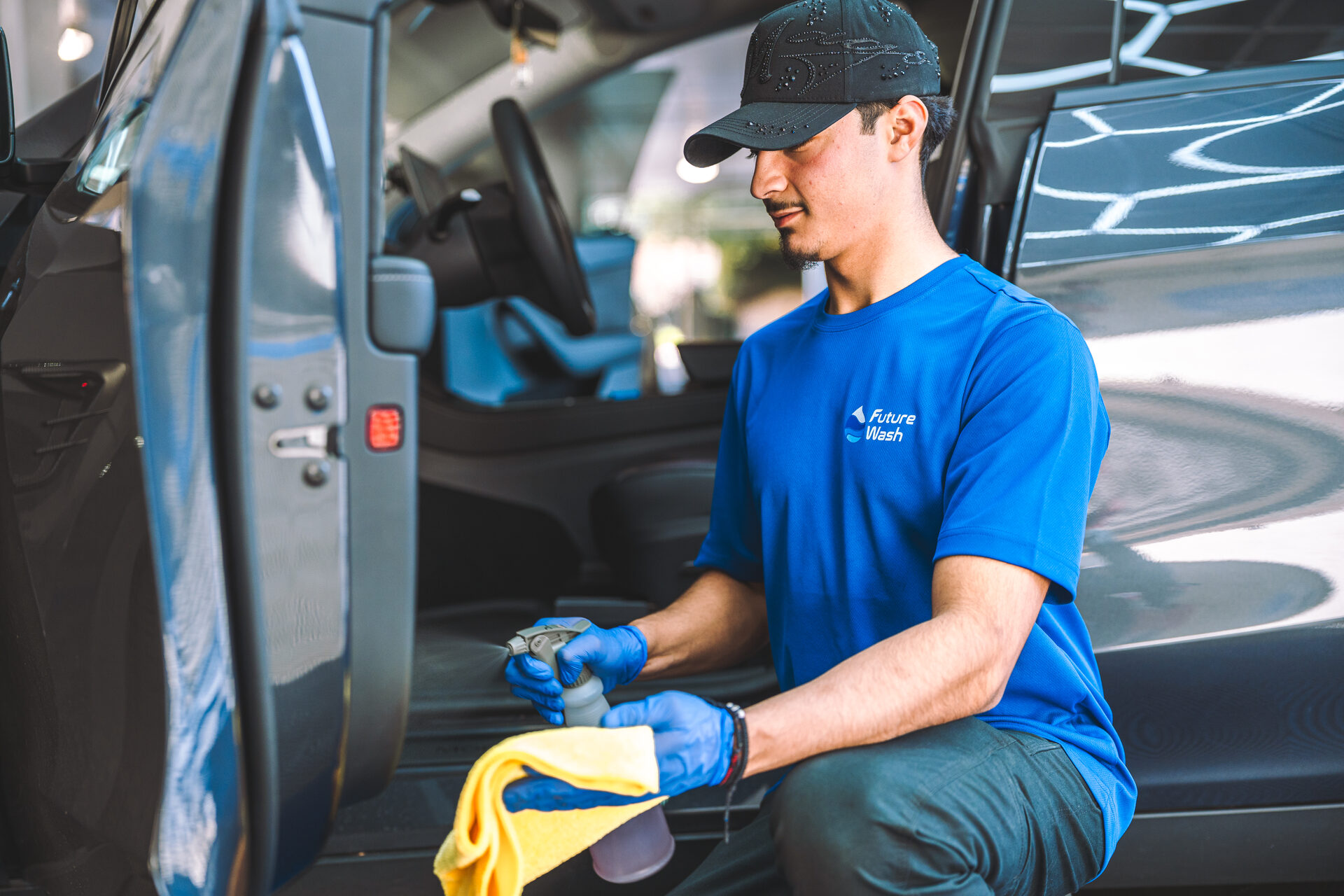 Future Wash technician in blue gloves preparing spray bottle and microfiber cloth to detail a dark SUV interior
